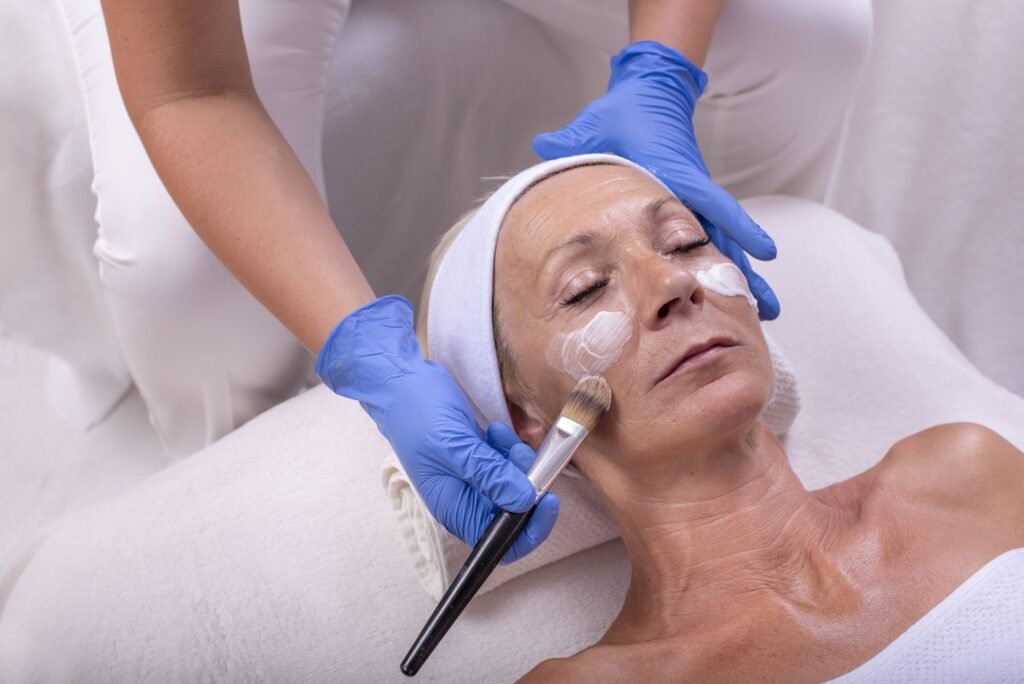 Seorang wanita dewasa sedang menjalani perawatan anti aging dengan aplikasi krim wajah di klinik kecantikan oleh terapis profesional.